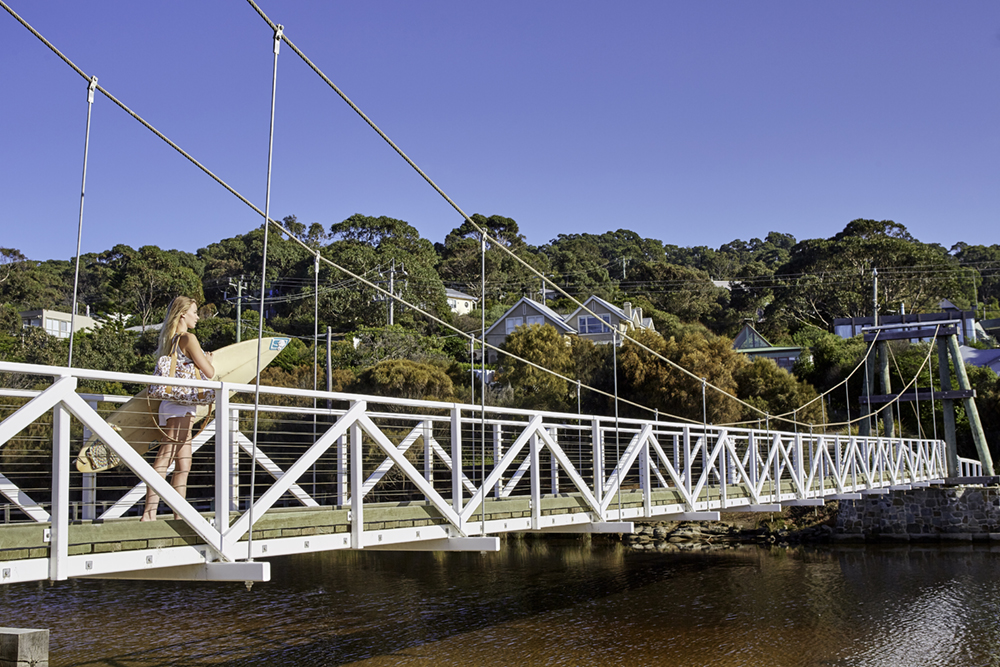 Woman carrying surfboard on Lorne swing bridge